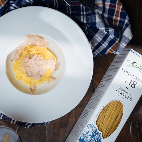 Piatto di Tagliolini con Tartufo tartufo bianco d'alba su tovaglia a quadri blu e rossa con accanto confezione Tagliolino N.18 Tartuflangje