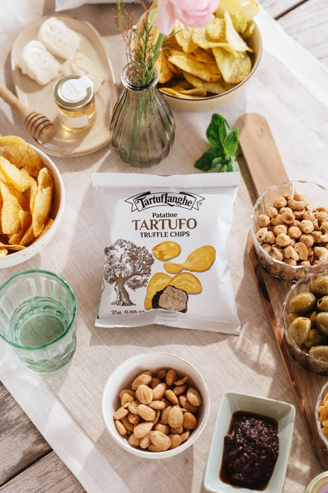 Confezione di patatine al tartufo Tartuflanghe su una tavola da aperitivo con chips, olive, frutta secca e salsa al tartufo.